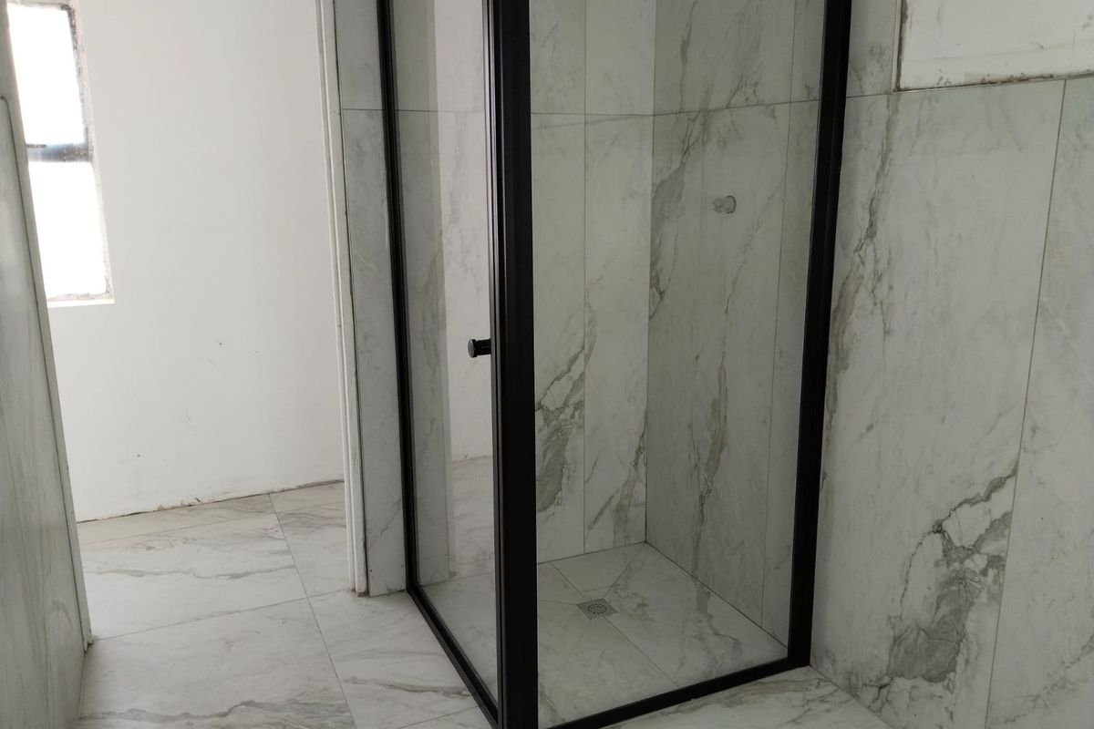 A modern bathroom featuring a walk-in shower with a sleek black-framed glass enclosure and contemporary marble-look wall and floor tiling.
