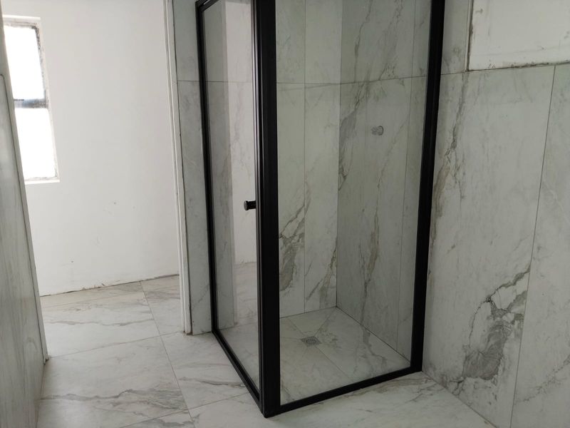 A modern bathroom featuring a walk-in shower with a sleek black-framed glass enclosure and contemporary marble-look wall and floor tiling.