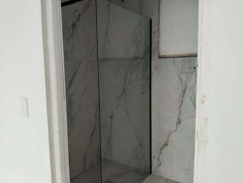 A modern walk-in shower featuring marble-look tiling and a glass screen, currently in an unfinished state with exposed wiring and incomplete door trim.