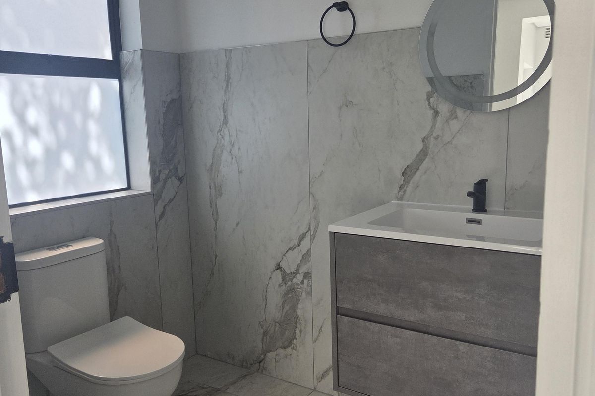 Modern bathroom featuring marble-look porcelain tiling, a wall-hung vanity with integrated basin, black fixtures, and a contemporary round LED mirror.
