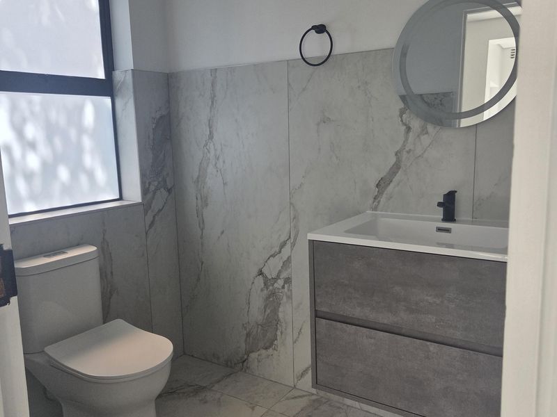Modern bathroom featuring marble-look porcelain tiling, a wall-hung vanity with integrated basin, black fixtures, and a contemporary round LED mirror.