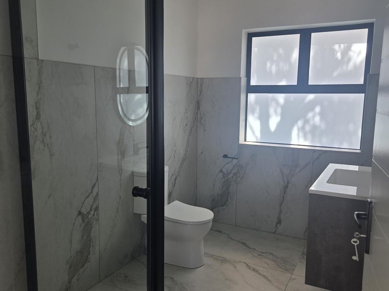 Modern bathroom featuring a walk-in shower with black-framed glass, wall-mounted vanity, and elegant marble-look floor and wall tiling.