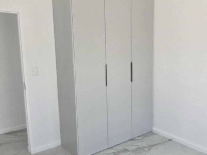 A bright, modern bedroom featuring sleek built-in wardrobes and high-quality marble-look floor tiles in a clean, minimalist space.