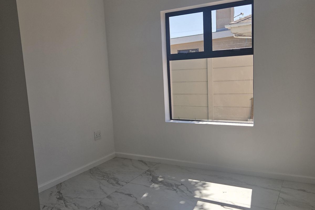 A bright, empty bedroom featuring modern marble-look porcelain floor tiles, neutral white walls, and a large aluminium-framed window.