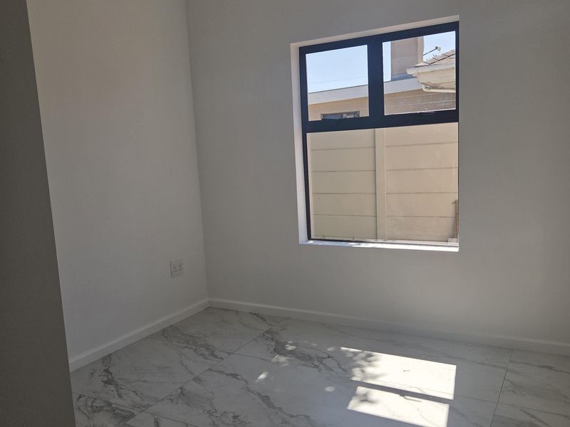 A bright, empty bedroom featuring modern marble-look porcelain floor tiles, neutral white walls, and a large aluminium-framed window.