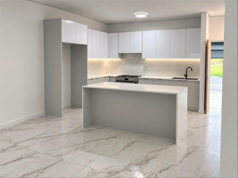 Modern kitchen featuring sleek white cabinetry, stone countertops, a central island, and high-quality marble-look porcelain floor tiles.