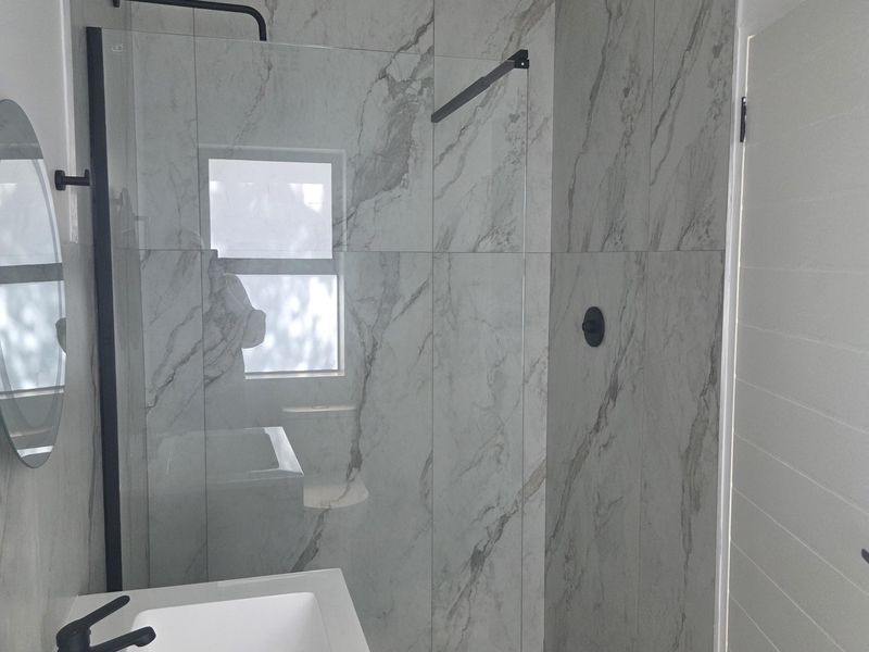 Modern bathroom featuring a walk-in shower with glass screen, marble-look tiling, and contemporary black matte fixtures.