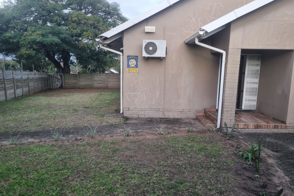 Rear exterior view of the property featuring a lawn, paved walkway, security gate, and wall-mounted air conditioning unit.