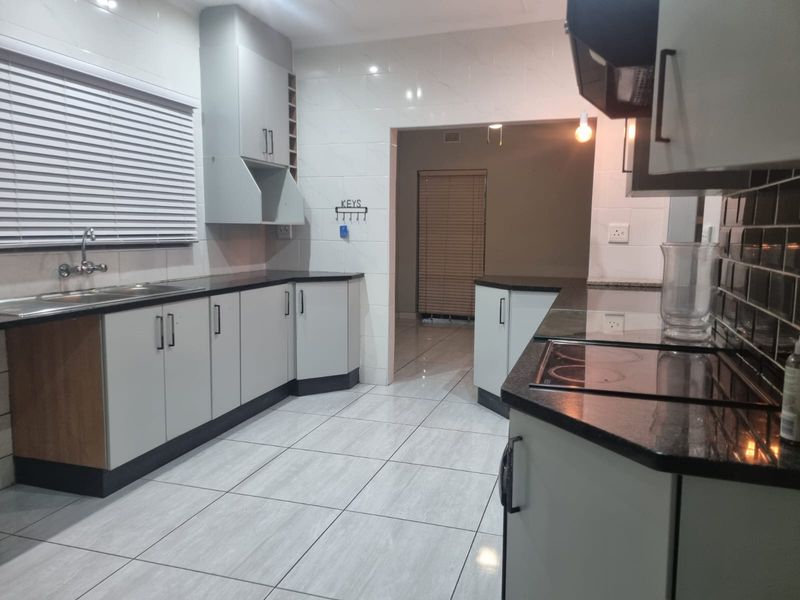 A clean, modern kitchen featuring light-toned cabinetry, dark granite countertops, an electric hob with extractor, and tiled finishes throughout.