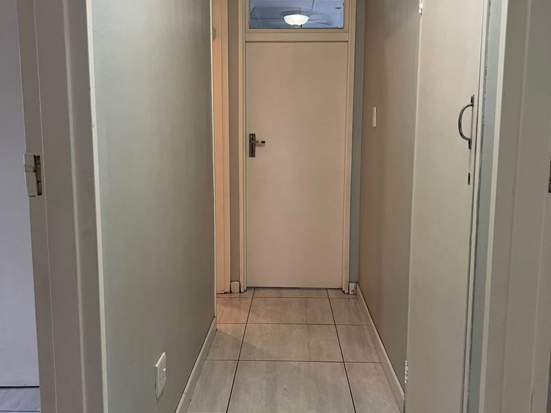 A clean and functional hallway featuring neutral tiled flooring, a built-in storage cupboard, and a classic door with a transom window.