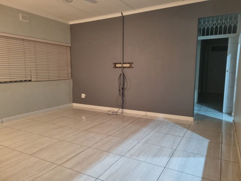 An empty living room featuring tiled flooring, venetian blinds, and a wall-mounted TV bracket with exposed cabling.