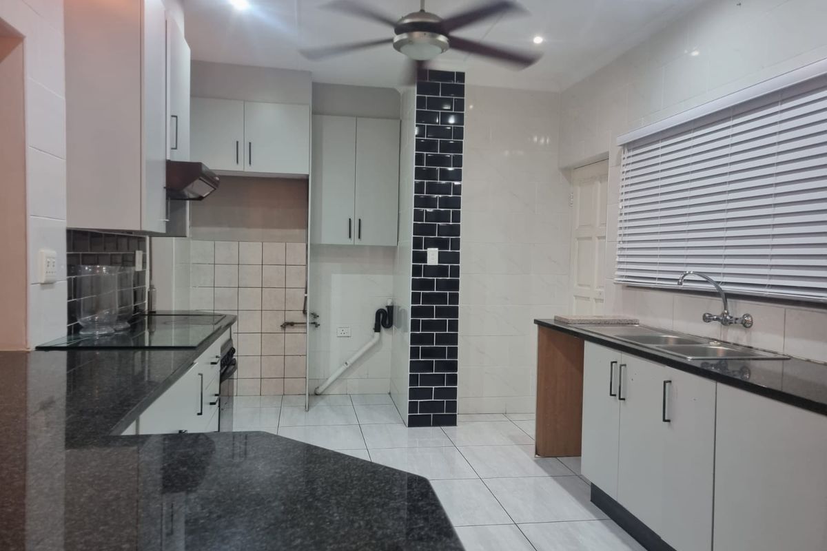 A functional kitchen featuring granite countertops, white cabinetry, a double basin sink, and tiled flooring with a modern subway tile accent wall.