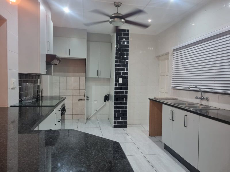A functional kitchen featuring granite countertops, white cabinetry, a double basin sink, and tiled flooring with a modern subway tile accent wall.