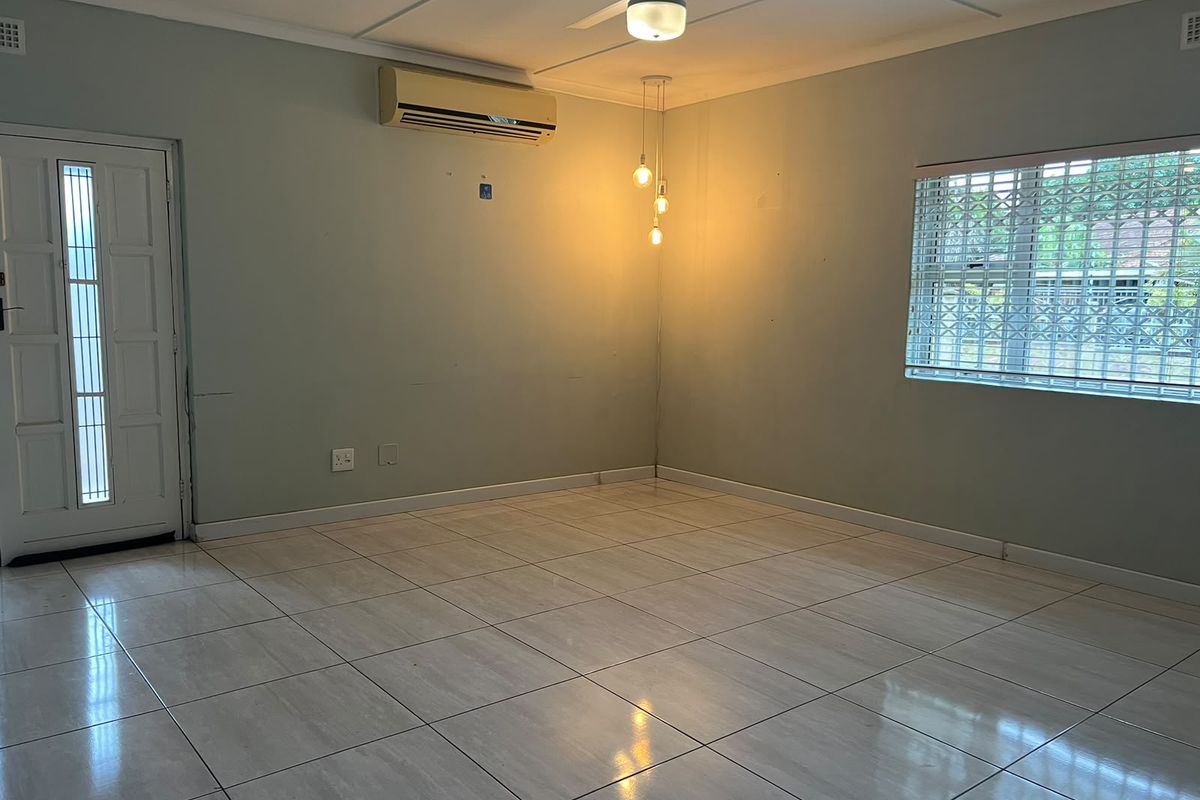 An empty living room featuring tiled flooring, a ceiling fan, split-system air conditioning, and security features on the door and window.
