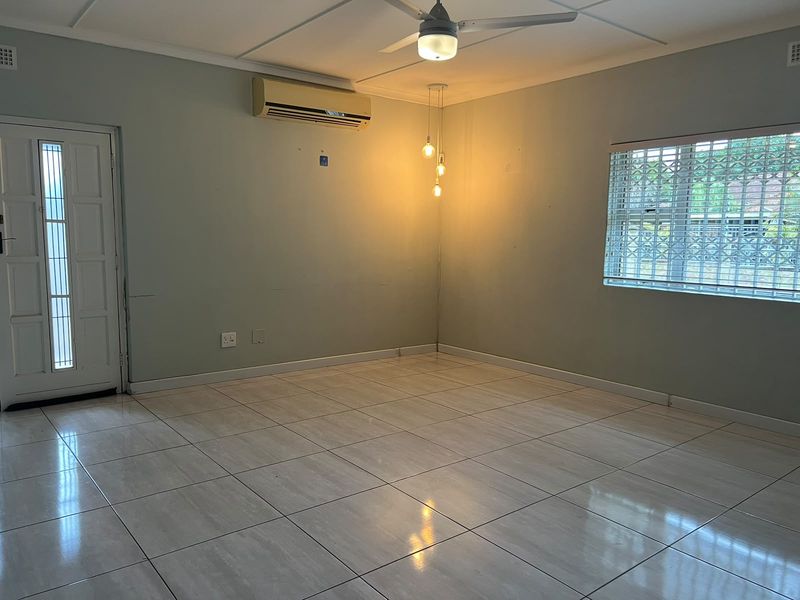 An empty living room featuring tiled flooring, a ceiling fan, split-system air conditioning, and security features on the door and window.