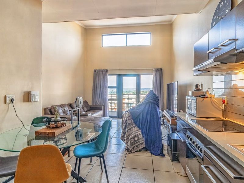 Open-plan living and kitchen area featuring tiled floors, high ceilings with a clerestory window, and direct access to a balcony through sliding glass doors.