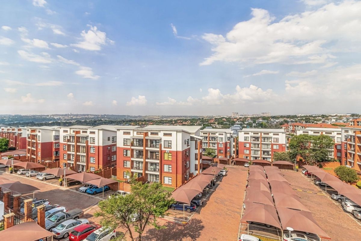 An elevated aerial view of a residential apartment complex featuring multiple buildings, paved parking areas, and covered carports.