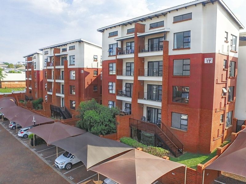 Aerial view of a multi-story apartment complex featuring brick facades, private balconies, and dedicated shade-cloth parking bays for residents.