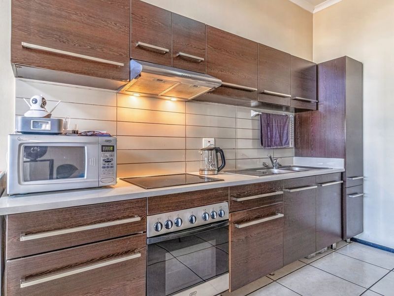 A functional kitchen featuring dark wood-finish cabinetry, a built-in oven with electric hob, extractor fan, and a tiled backsplash.