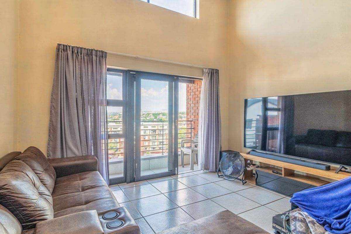 Spacious living room featuring double volume ceilings, tiled flooring, and large sliding glass doors that open onto a private balcony with urban views.
