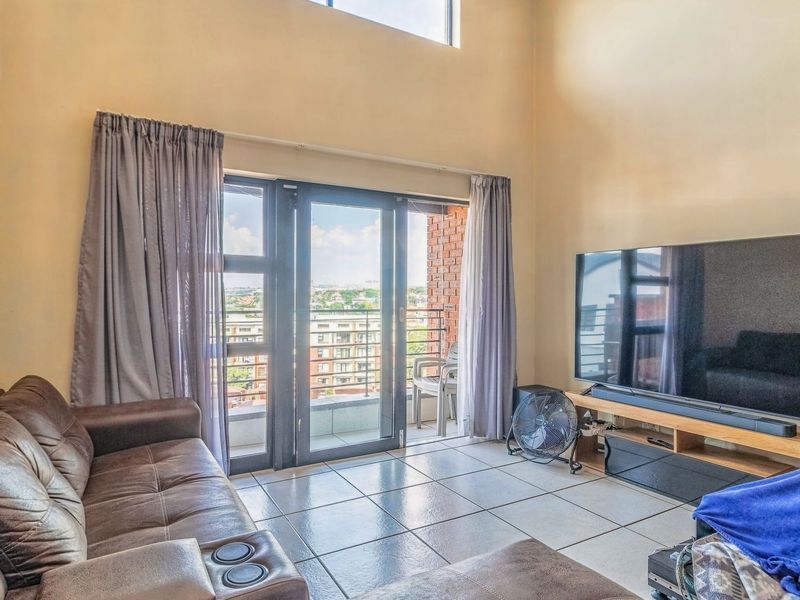 Spacious living room featuring double volume ceilings, tiled flooring, and large sliding glass doors that open onto a private balcony with urban views.