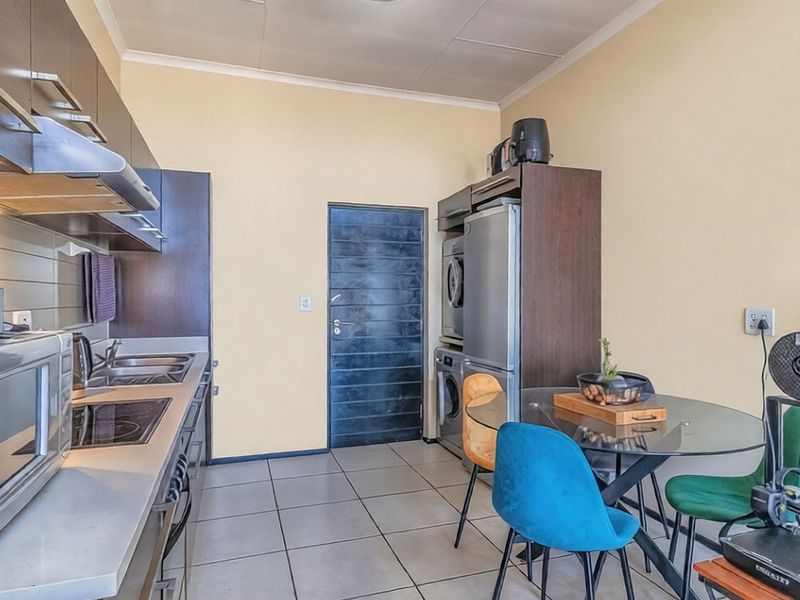 A functional kitchen featuring dark cabinetry, integrated hob, extractor fan, and dedicated space for laundry appliances, finished with neutral tiled flooring.