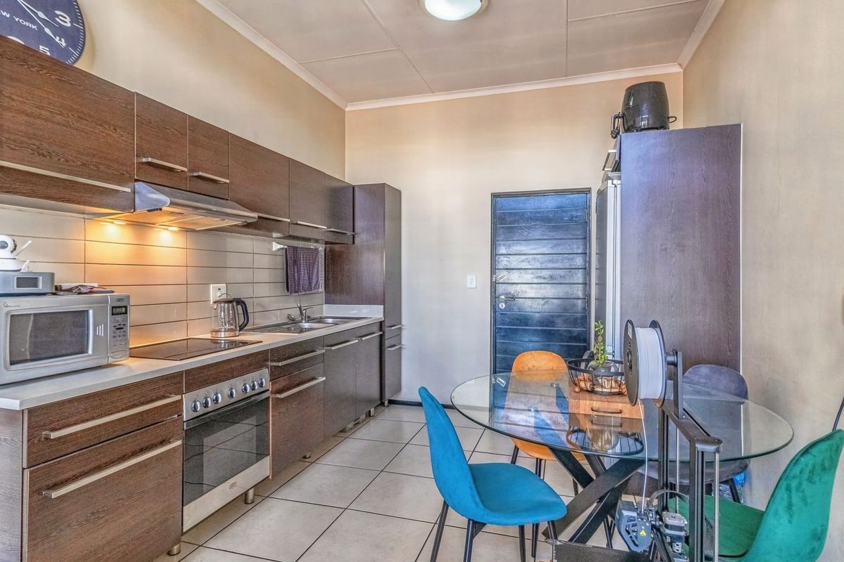 A functional kitchen featuring dark wood cabinetry, stainless steel appliances, tiled backsplash, and tiled flooring, with an adjacent dining area.