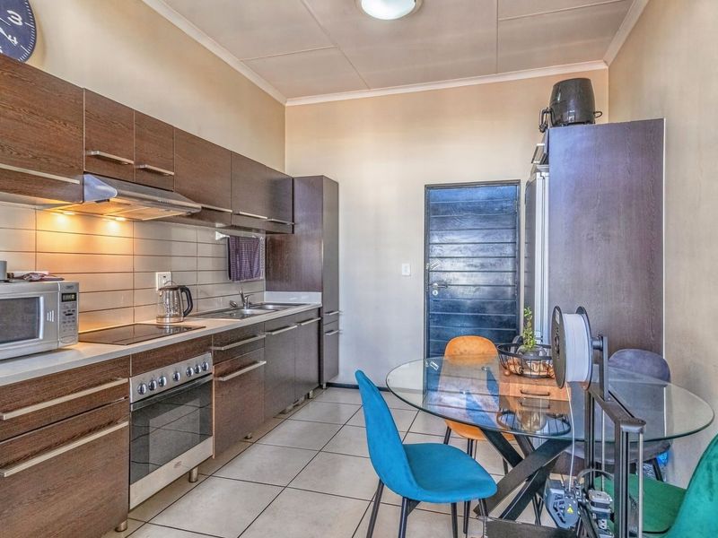 A functional kitchen featuring dark wood cabinetry, stainless steel appliances, tiled backsplash, and tiled flooring, with an adjacent dining area.