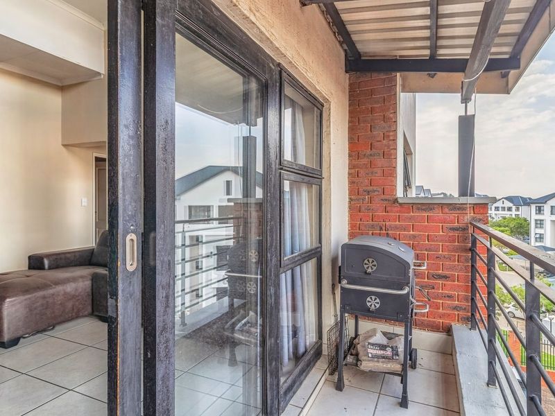 A covered balcony featuring tiled flooring, exposed brick accents, and a metal railing, providing a seamless transition from the interior living space.