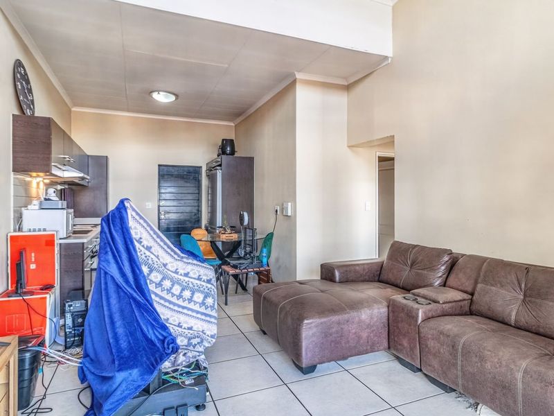 Open-plan living area featuring tiled flooring and a compact kitchen with built-in cabinetry and an extractor fan.