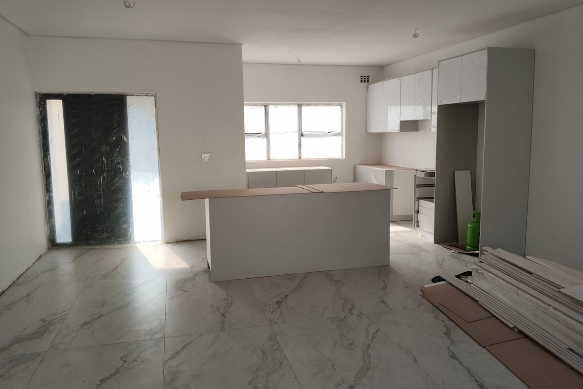 An open-plan kitchen and living area under construction, featuring modern marble-look floor tiles and newly installed white cabinetry.