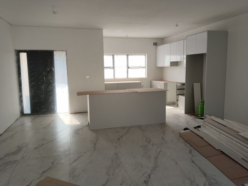 An open-plan kitchen and living area under construction, featuring modern marble-look floor tiles and newly installed white cabinetry.