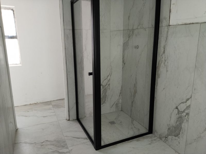 Modern bathroom featuring a walk-in shower with a sleek black frame and contemporary marble-look wall and floor tiling.
