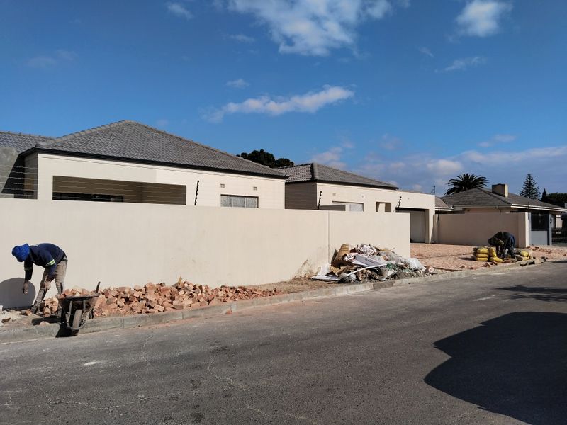 Front exterior view of a townhouse complex showing ongoing construction work, perimeter walling with electric fencing, and paved driveway areas.