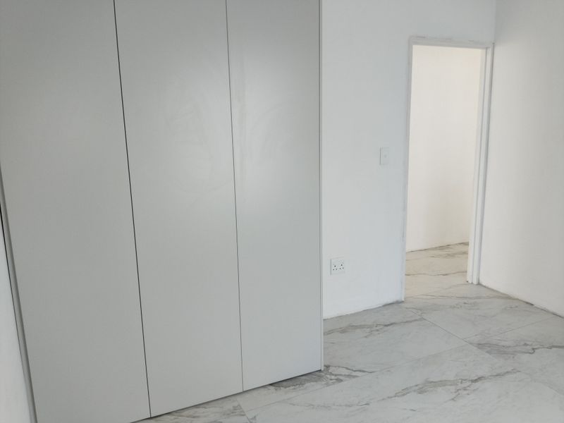 A clean, empty bedroom featuring modern marble-look floor tiles and built-in cupboards, offering a neutral canvas for interior design.