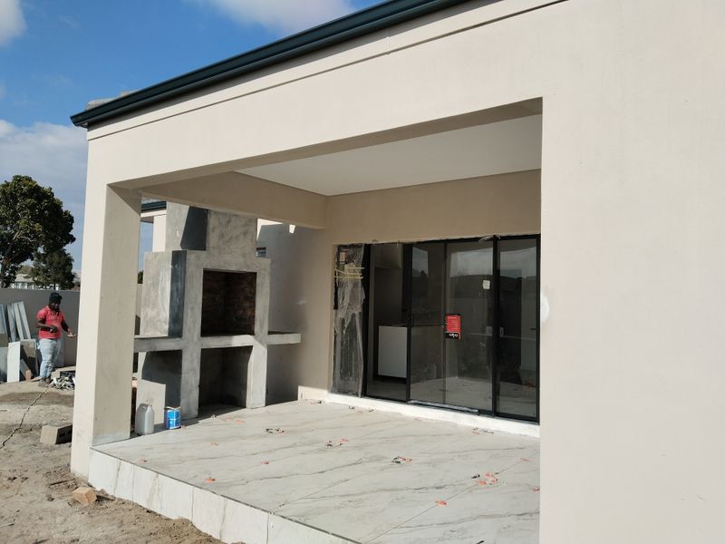 A covered patio featuring a built-in braai and large sliding glass doors, currently in the final stages of construction.