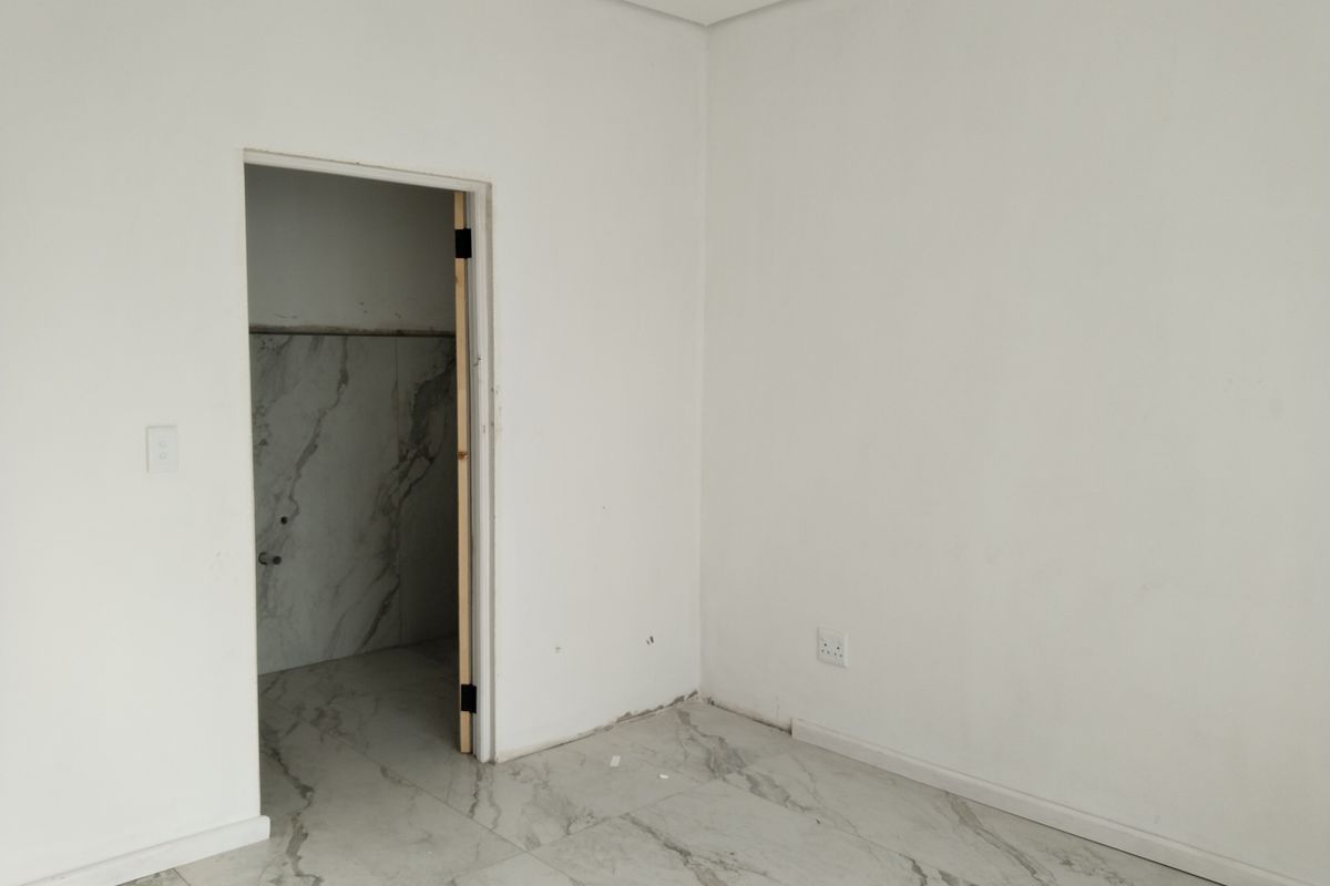 An empty bedroom featuring modern marble-look floor tiles and neutral walls, currently undergoing final finishing touches.