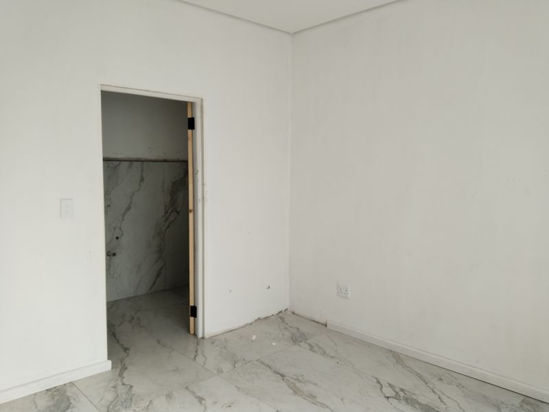An empty bedroom featuring modern marble-look floor tiles and neutral walls, currently undergoing final finishing touches.