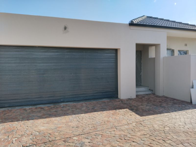 Front elevation of the townhouse featuring a paved driveway, a large sectional garage door, and a modern plastered facade.