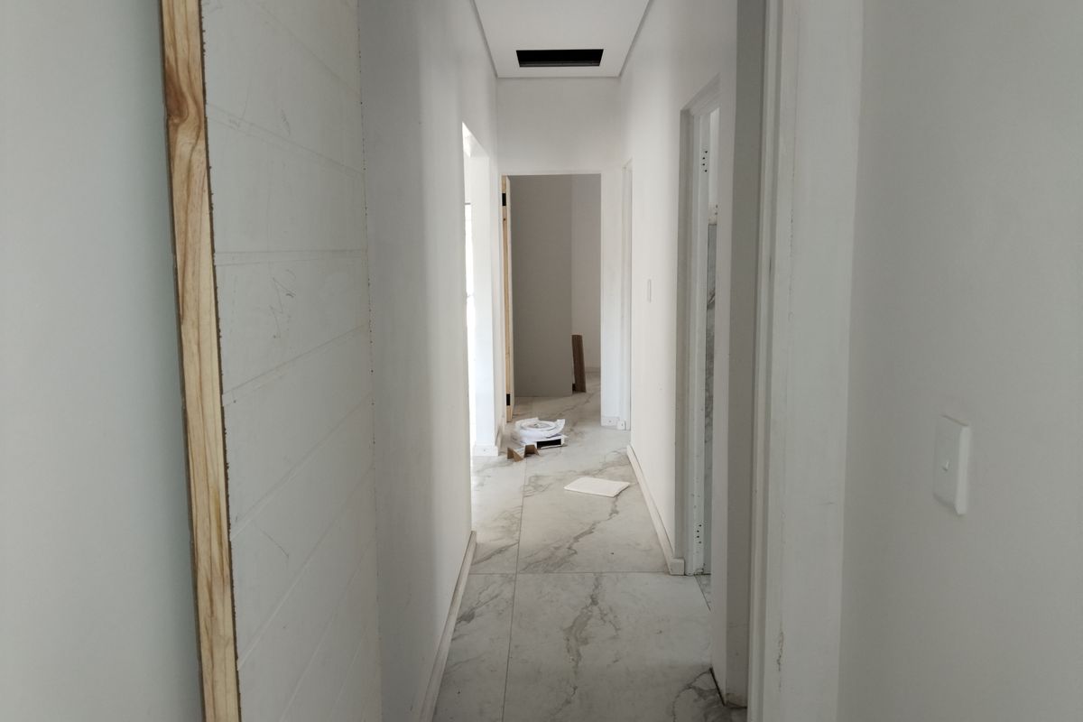 A narrow hallway featuring large format marble-look floor tiles and unfinished door frames, currently in a state of renovation.
