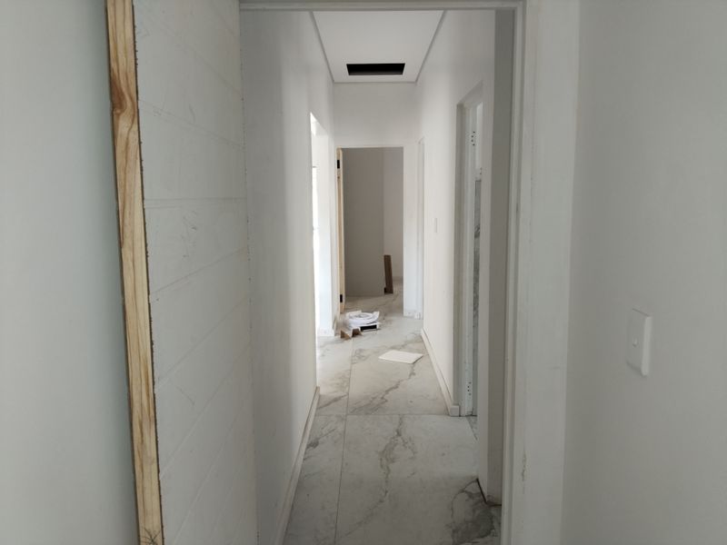 A narrow hallway featuring large format marble-look floor tiles and unfinished door frames, currently in a state of renovation.