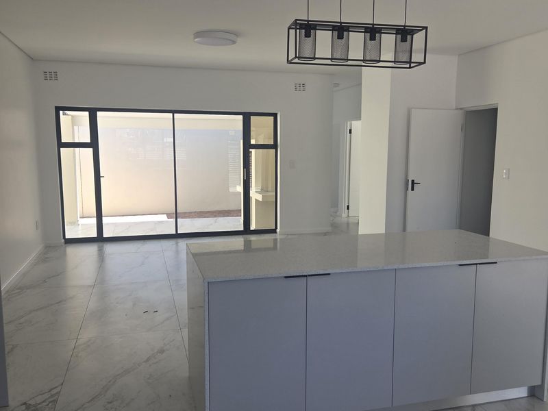 Modern open-plan living area featuring a sleek kitchen island, large format marble-look floor tiles, and expansive sliding glass doors leading to the patio.