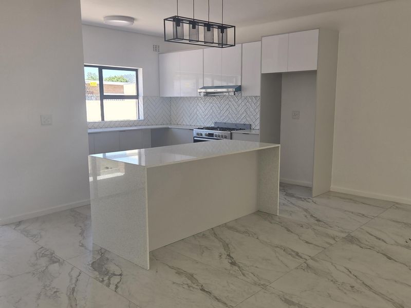 Modern, bright kitchen featuring a central island, quartz countertops, herringbone backsplash, and high-quality marble-look floor tiles in an open-plan layout.