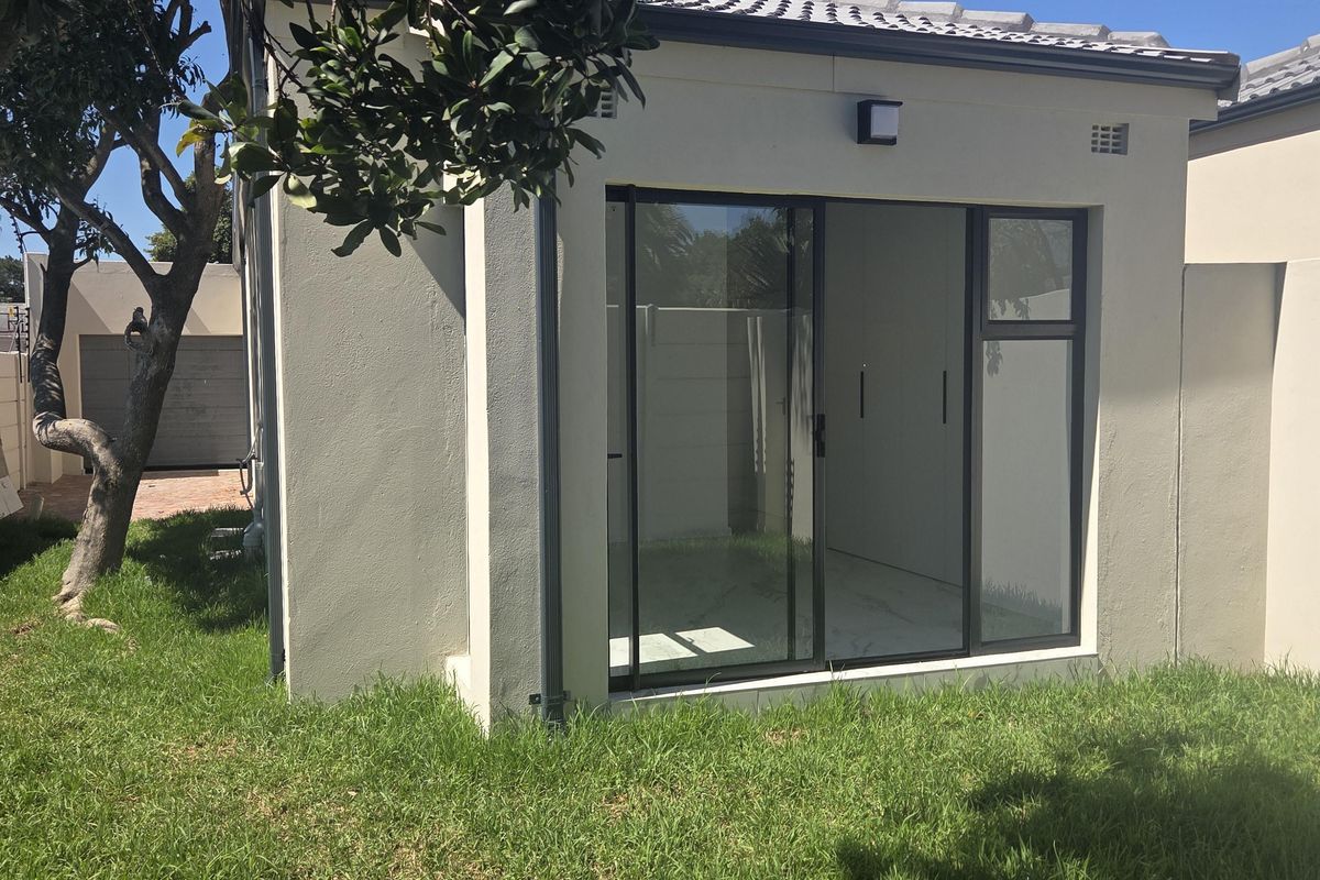 A view of the rear exterior of the property featuring a modern outbuilding with a tiled roof and sliding glass doors set in a garden.