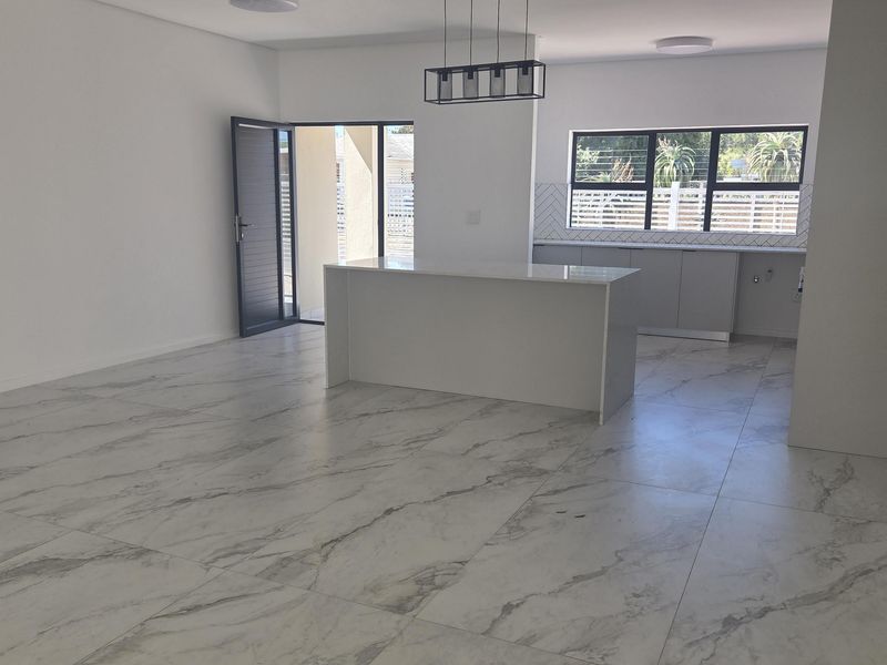 Spacious open-plan living and kitchen area featuring modern marble-look floor tiles, a central kitchen island, and contemporary finishes throughout.