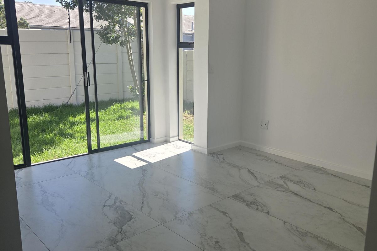Bright and modern living area featuring large marble-look floor tiles, sleek black aluminium sliding doors, and direct access to the private garden.