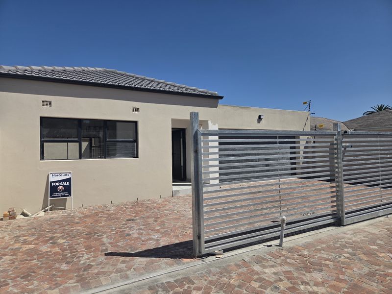 Front elevation of a single-story house featuring a paved driveway, sliding metal gate, and modern aluminium window frames.