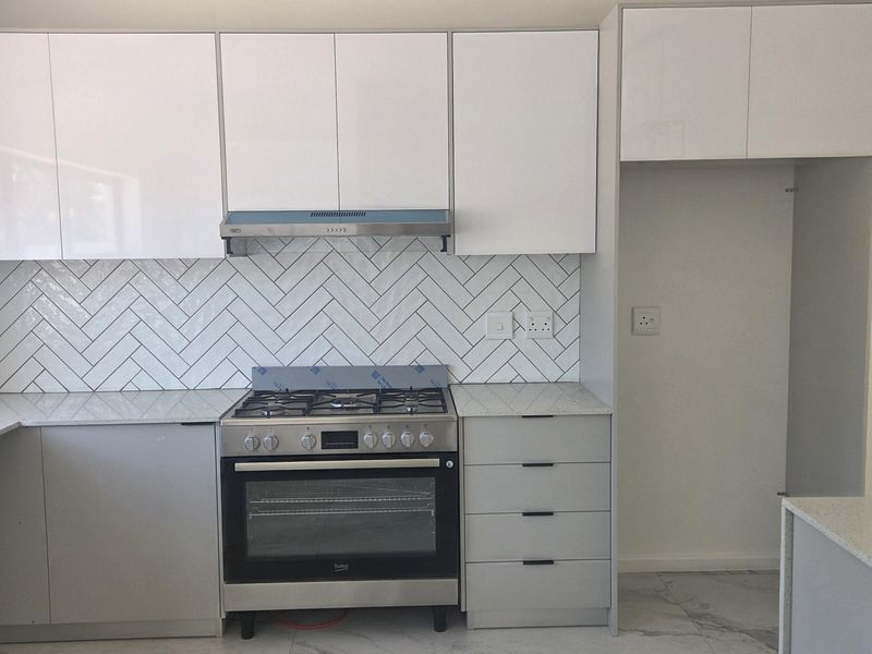 Modern kitchen featuring white cabinetry, herringbone tile backsplash, gas stove with extractor, quartz countertops, and elegant marble-look floor tiles.