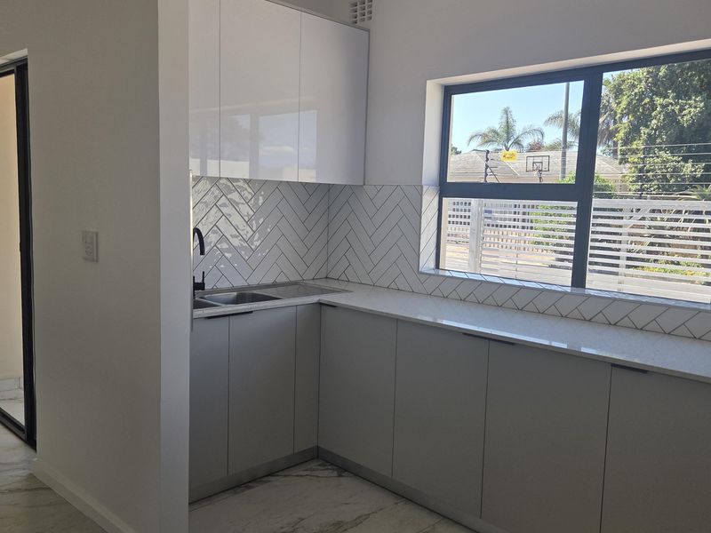 Modern kitchen featuring sleek handleless cabinetry, stone countertops, a stylish herringbone tile backsplash, and high-quality marble-look floor tiles with ample natural light.