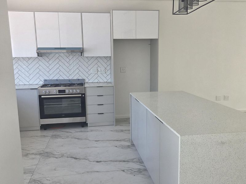 Modern kitchen featuring white cabinetry, stone countertops, a central island, herringbone backsplash, and marble-look floor tiles in a clean, contemporary space.